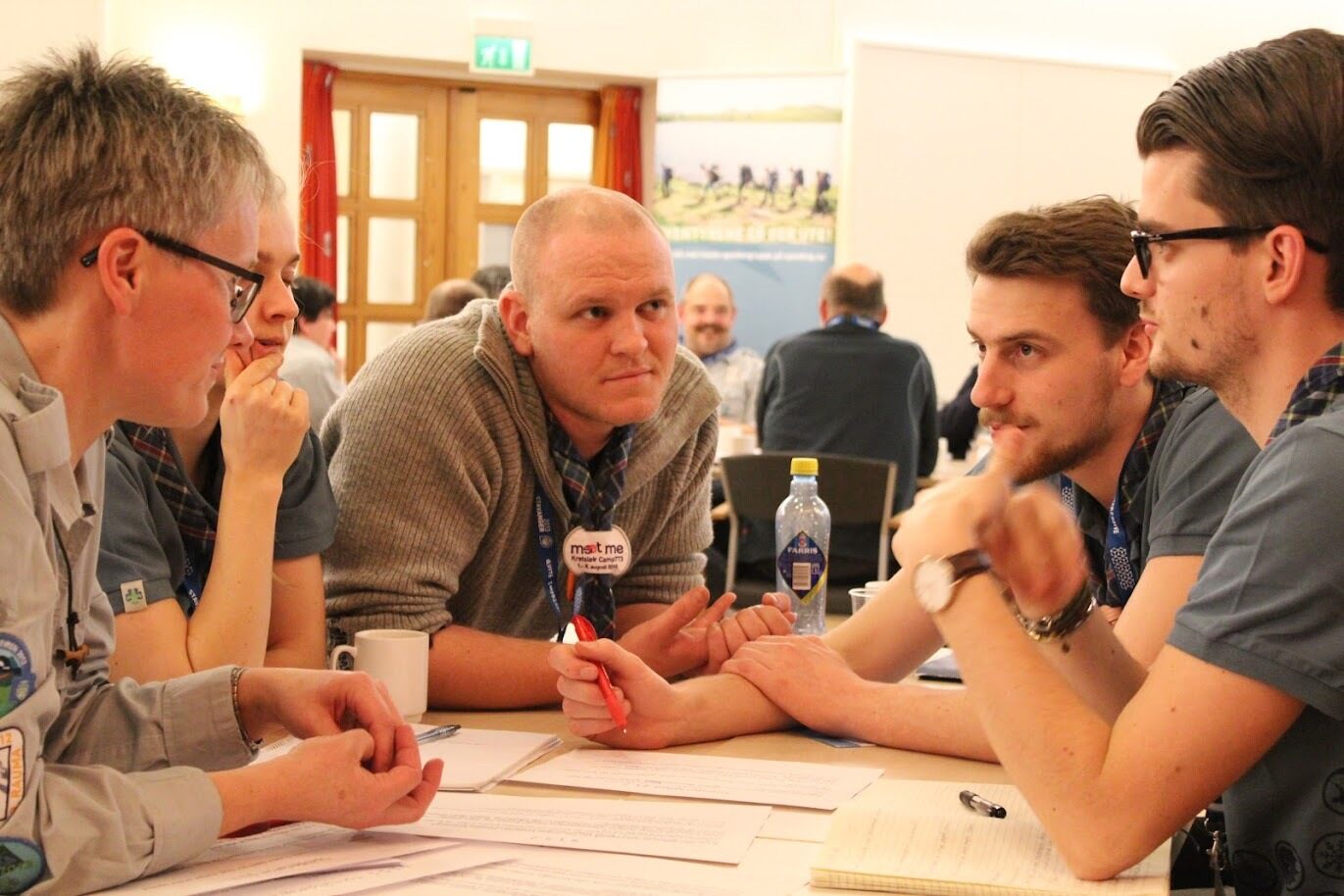 Ledere i speiderdrakt sitter rundt et bord og diskuterer