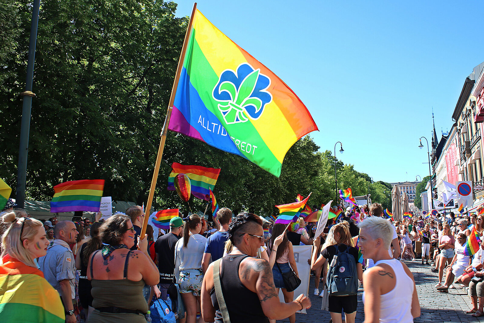 Speidere marsjerer i Pride-parade med regnbueflagg med speiderlogo og teksten «Alltid beredt»