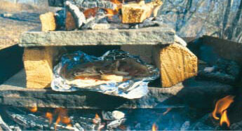 Syvsteinsovn med mat pakket i aluminiumsfolie i bakstekammeret og flammer under