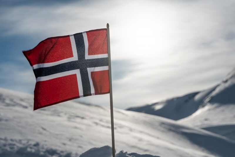 Norsk flagg vaier i vinden foran snødekte fjell