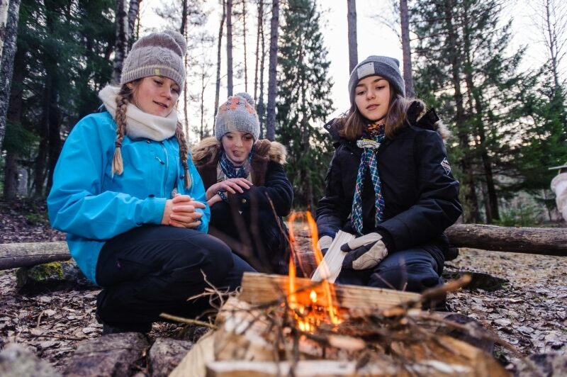 Tre speidere sitter rundt et bål i skogen