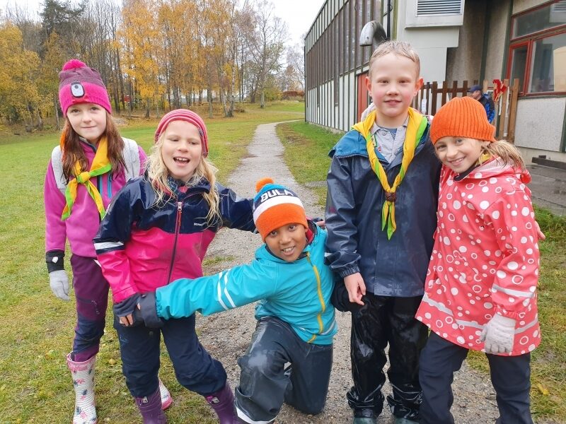 Fem speidere i regnklær som leker ute på gress