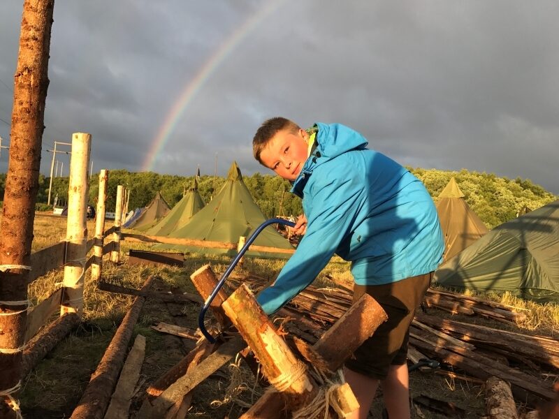 Gutt i blå jakke med en regnbue i bakgrunnen på en leirplass. Foto: Thomas Markento Andresen